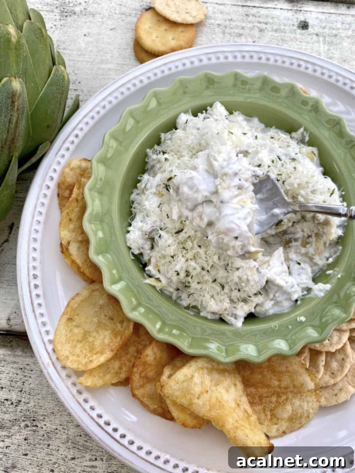 A large platter adorned with an array of chips and crackers, surrounding a small, inviting bowl of hot artichoke dip.