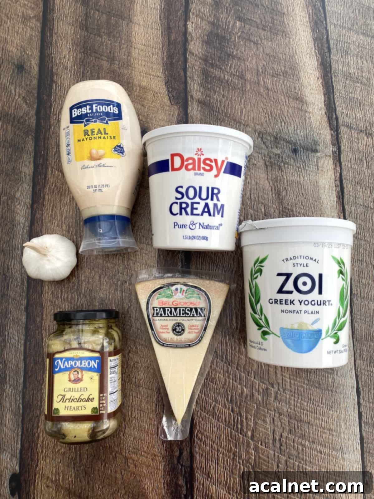 Essential ingredients for a delicious artichoke dip, neatly arranged on a rustic wooden plank.