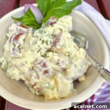 A vibrant bowl of creamy red potato salad, garnished with fresh celery, with a fork ready to serve and a napkin nearby.