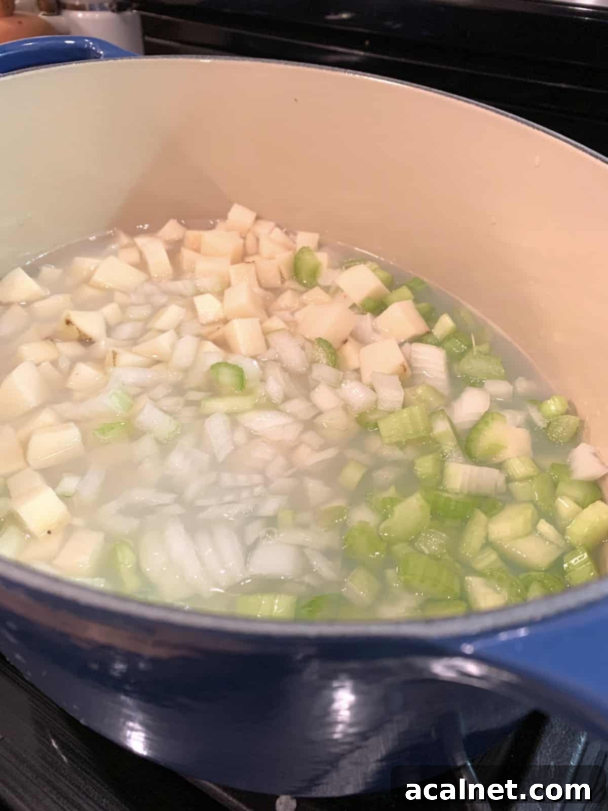 Various clam chowder ingredients simmering together in a large pot on a stovetop burner, showing the progress of cooking.