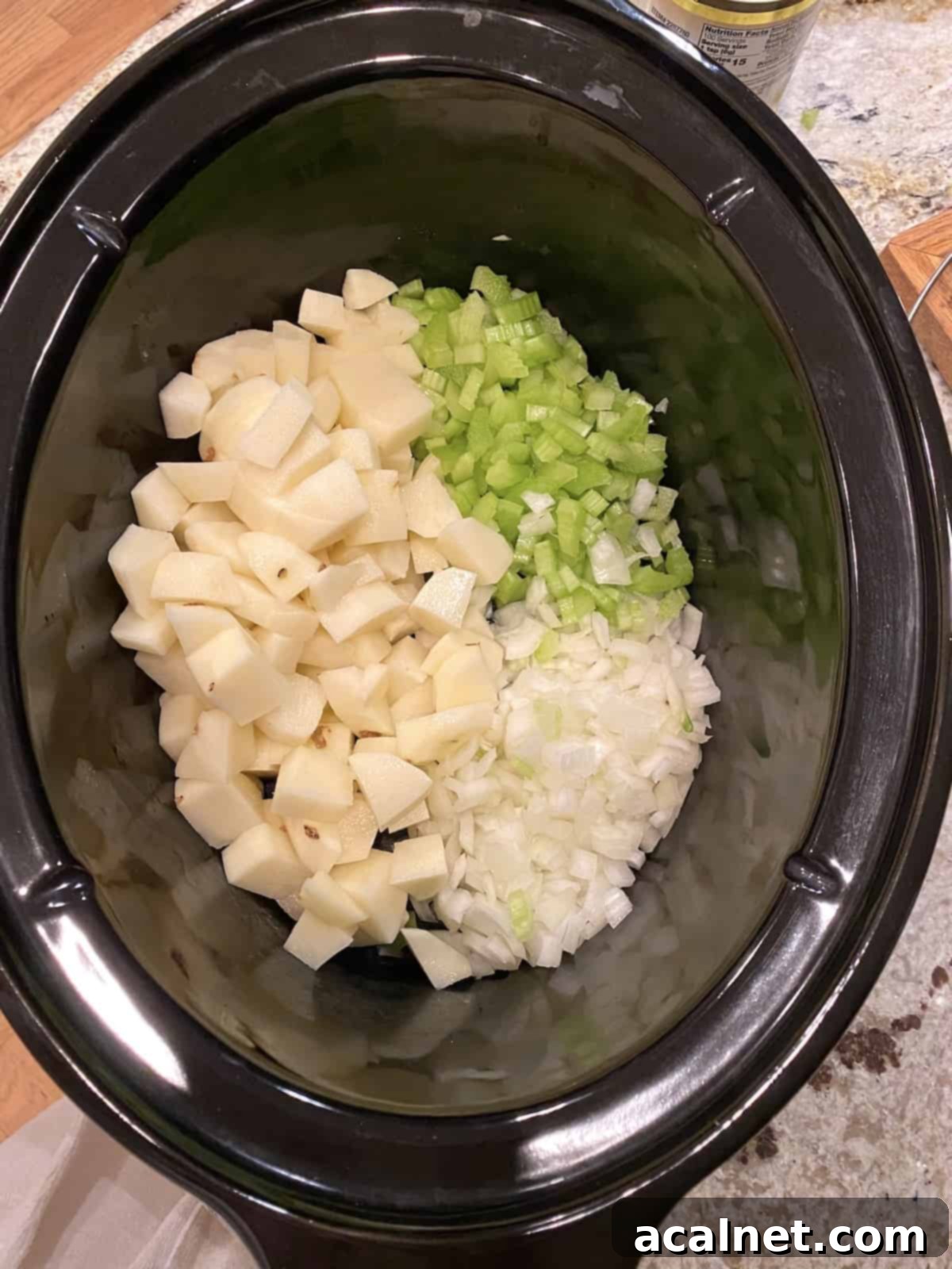 Diced potatoes, celery, and onions, along with chicken bouillon and clam juice, prepared in a large crockpot, ready for slow cooking.