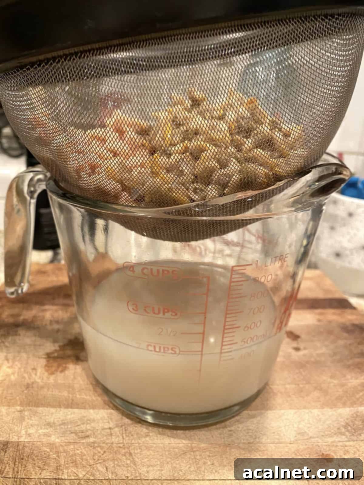 Canned clams being drained in a small strainer, with the precious clam juice collecting in a glass measuring cup below.