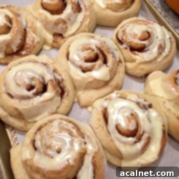 Orange rolls with icing on parchment paper on a baking sheet.