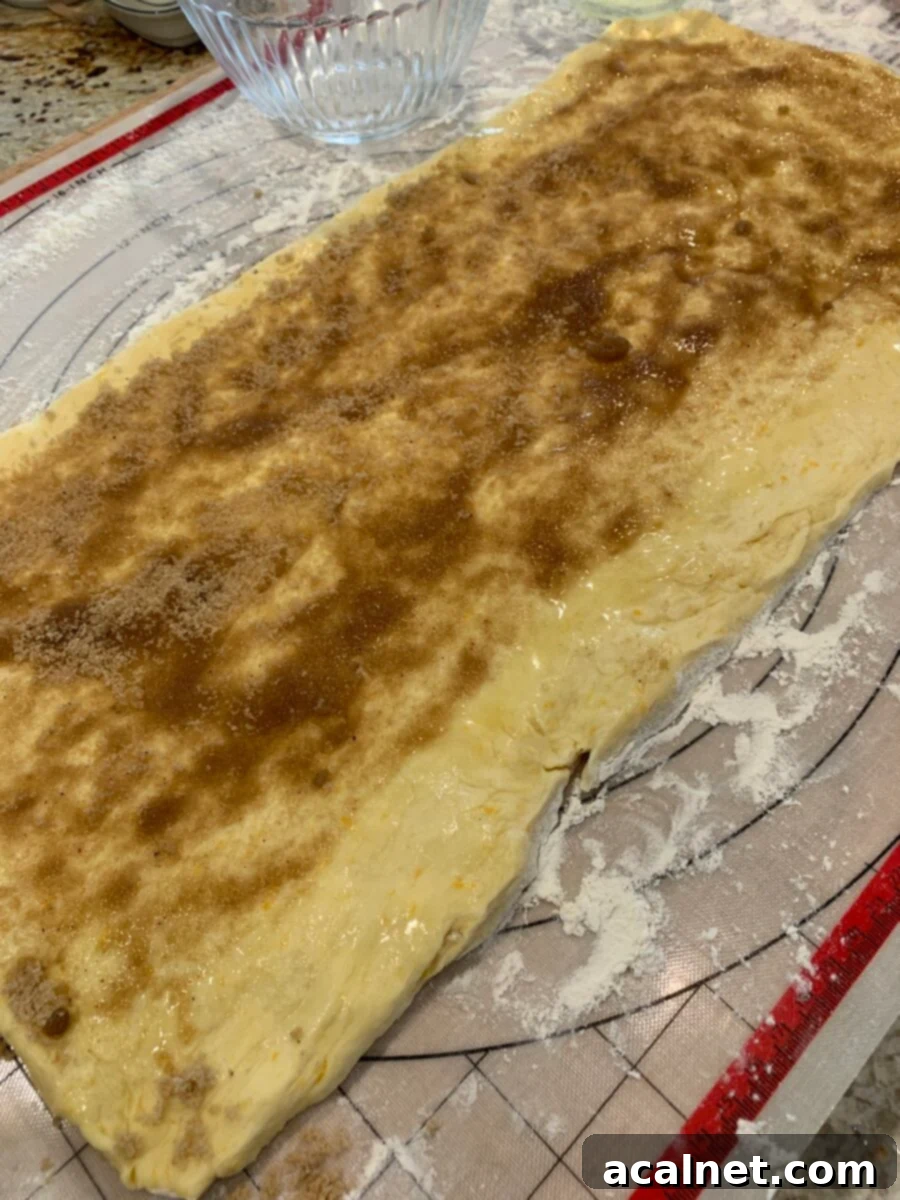 The smooth sweet roll dough is generously covered with a rich cinnamon filling, leaving a small border around the edges to prevent spillage when rolled.