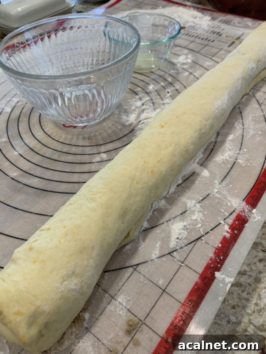 The sweet roll dough, now filled, is shown tightly rolled into a long, uniform cylinder, ready for slicing into individual portions.