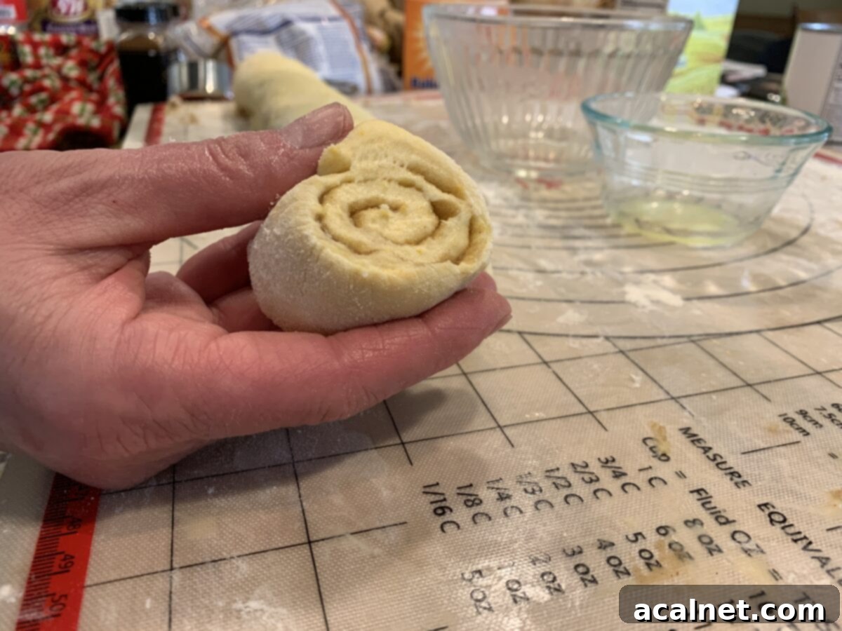 Perfectly sliced raw cinnamon roll dough, showcasing distinct spirals of filling, nestled on a baking sheet, ready for its final proofing before baking.