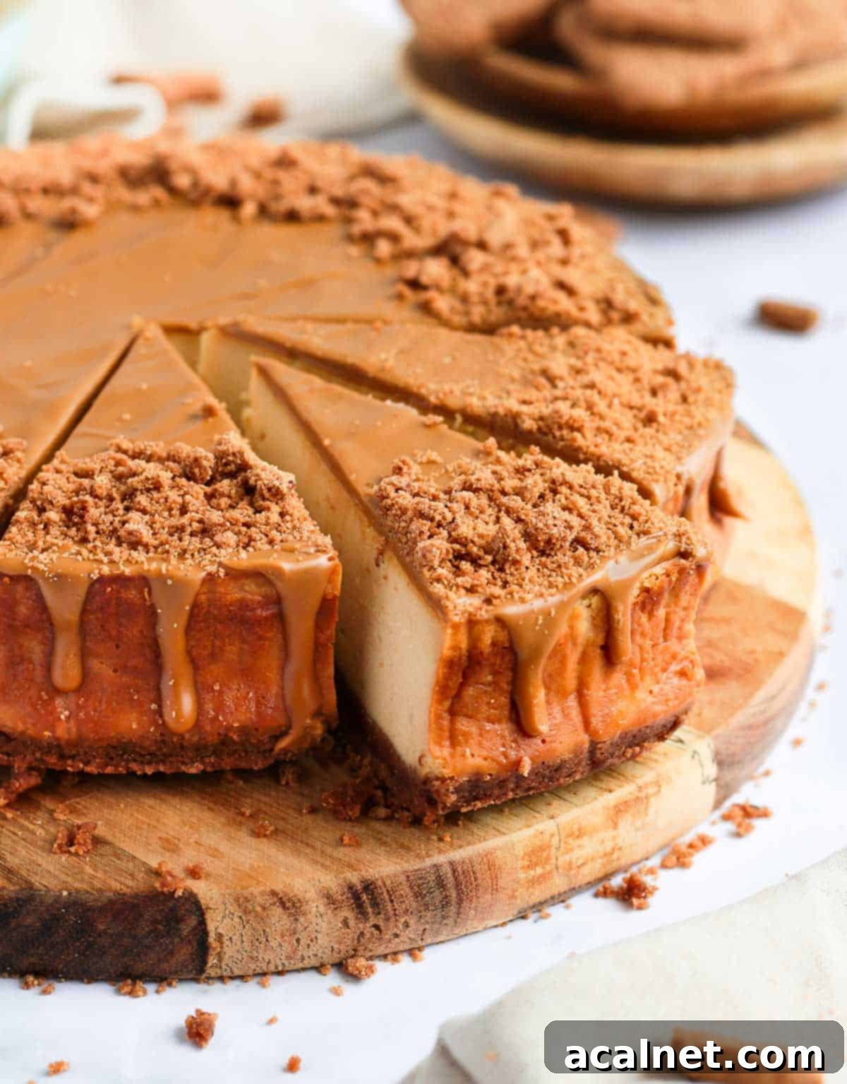Side view of the baked Biscoff cheesecake on a wooden board with three slices already cut and served, revealing the distinct layers.