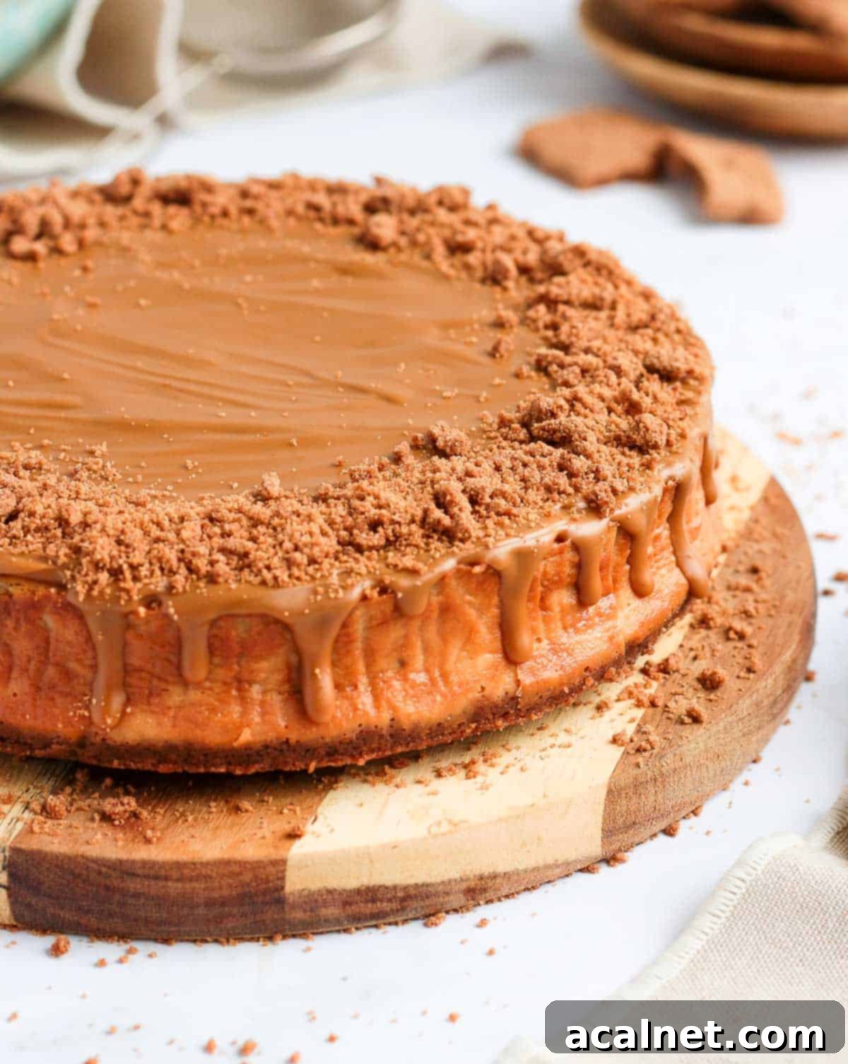 A side view of the baked Biscoff cheesecake resting on a round wooden board, highlighting its height and layers.
