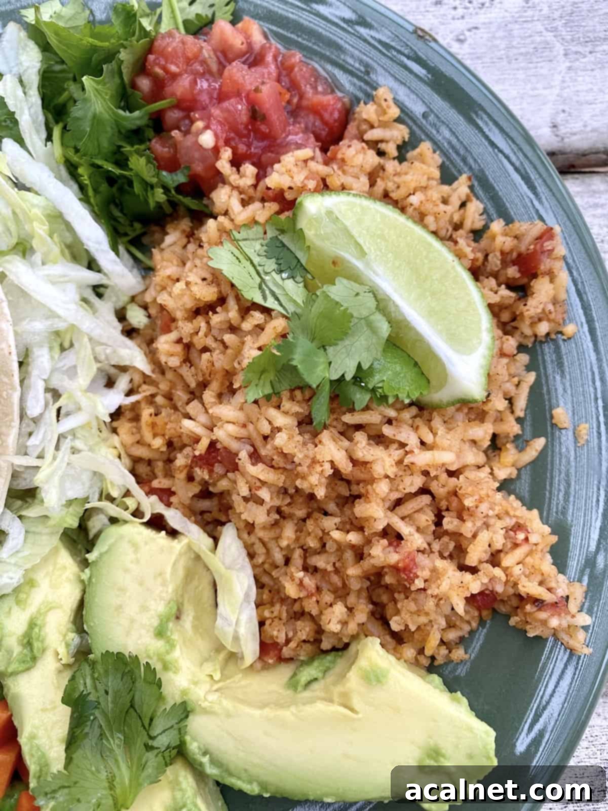 Mexican rice on a plate with avocado on the side, topped with lime.