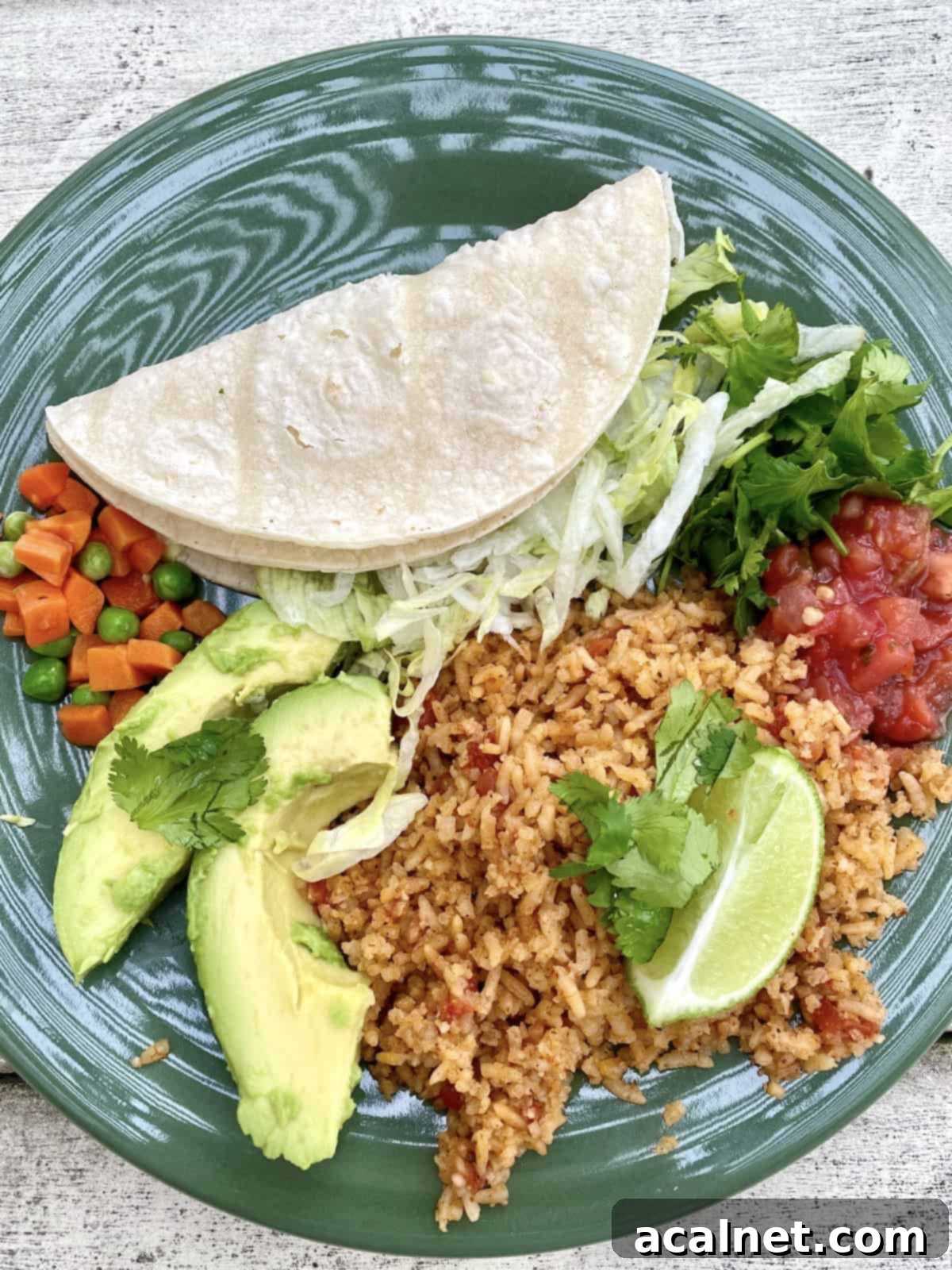 A plate with a serving of Mexican rice, topped with lime and avocado, peas and carrots and salsa on the side.