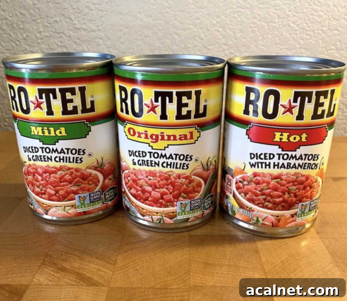 Three cans of Rotel lined up on a cutting board. Each a different variety for spiciness.