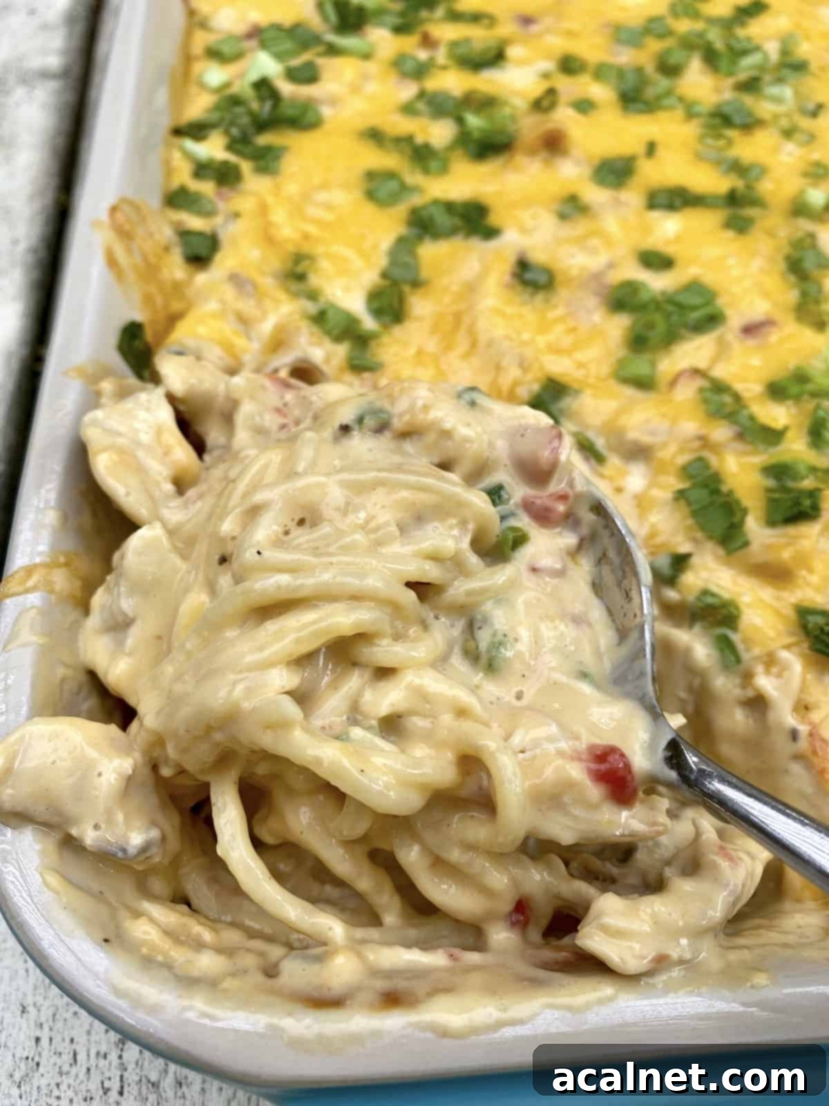 A spoon dishing up chicken spaghetti from a baking dish.