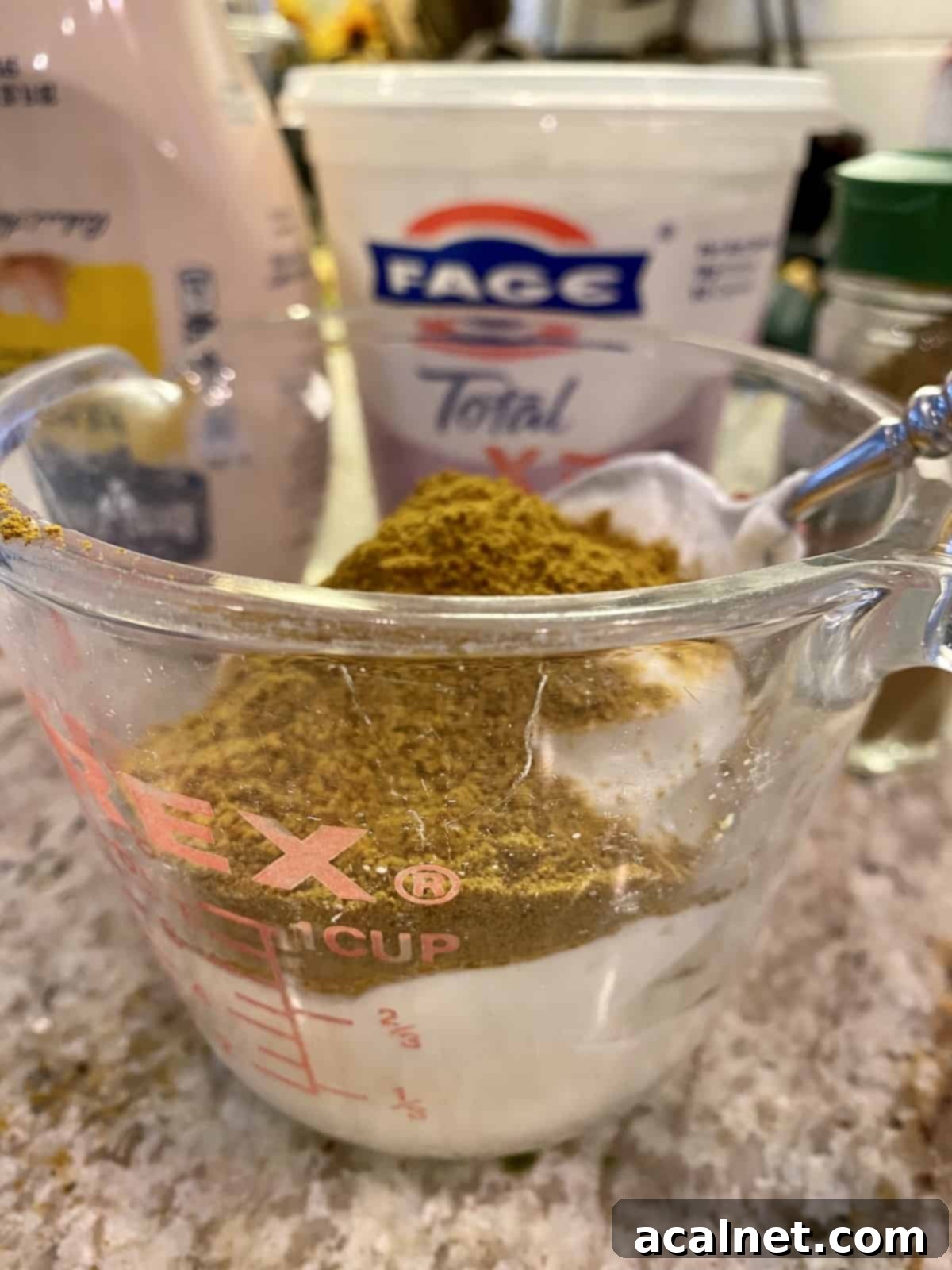 Curry powder on top of Greek yogurt and mayonnaise in a measuring cup.