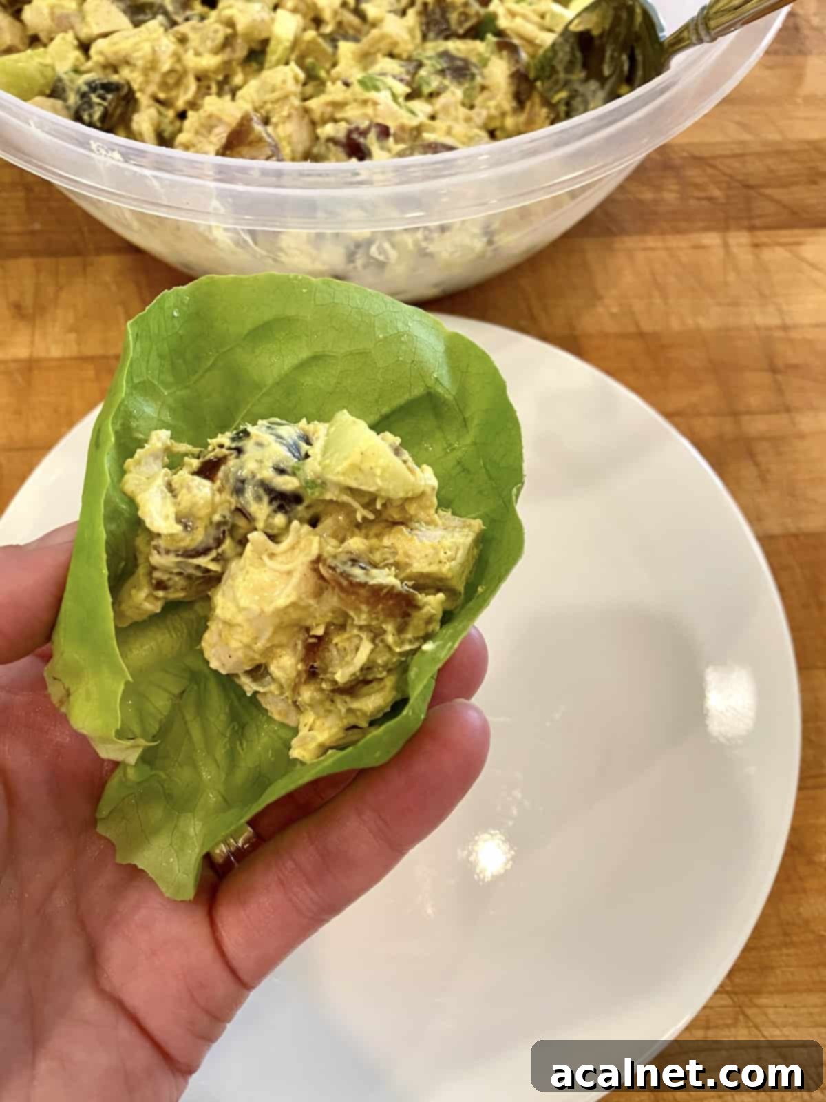 Chicken curry on a lettuce wrap, being held over a plate. 