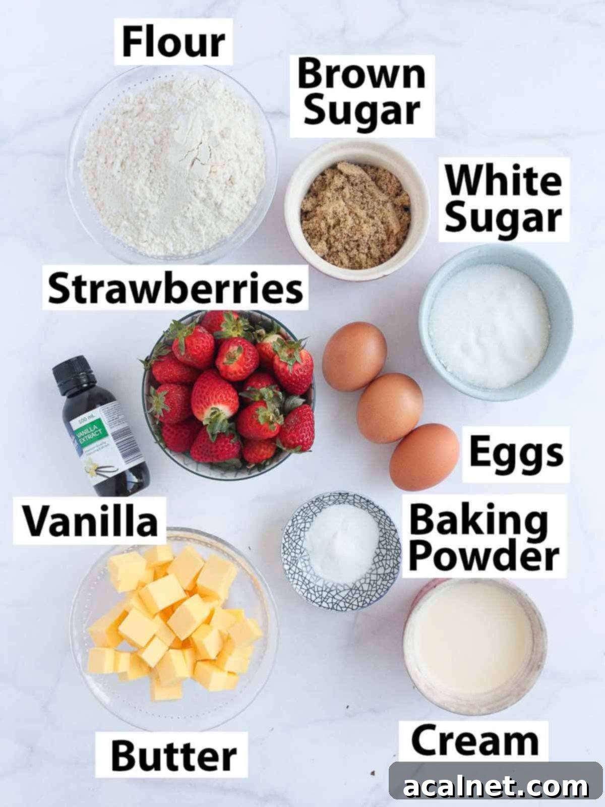 Various baking ingredients laid out on a white surface, including butter, eggs, flour, sugar, and fresh strawberries.