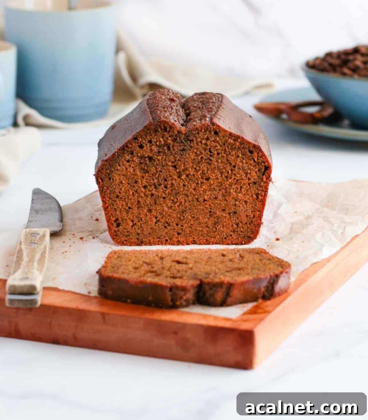 Half of a coffee loaf cake on a wooden board with one slice already cut and removed, showing the cake's interior.