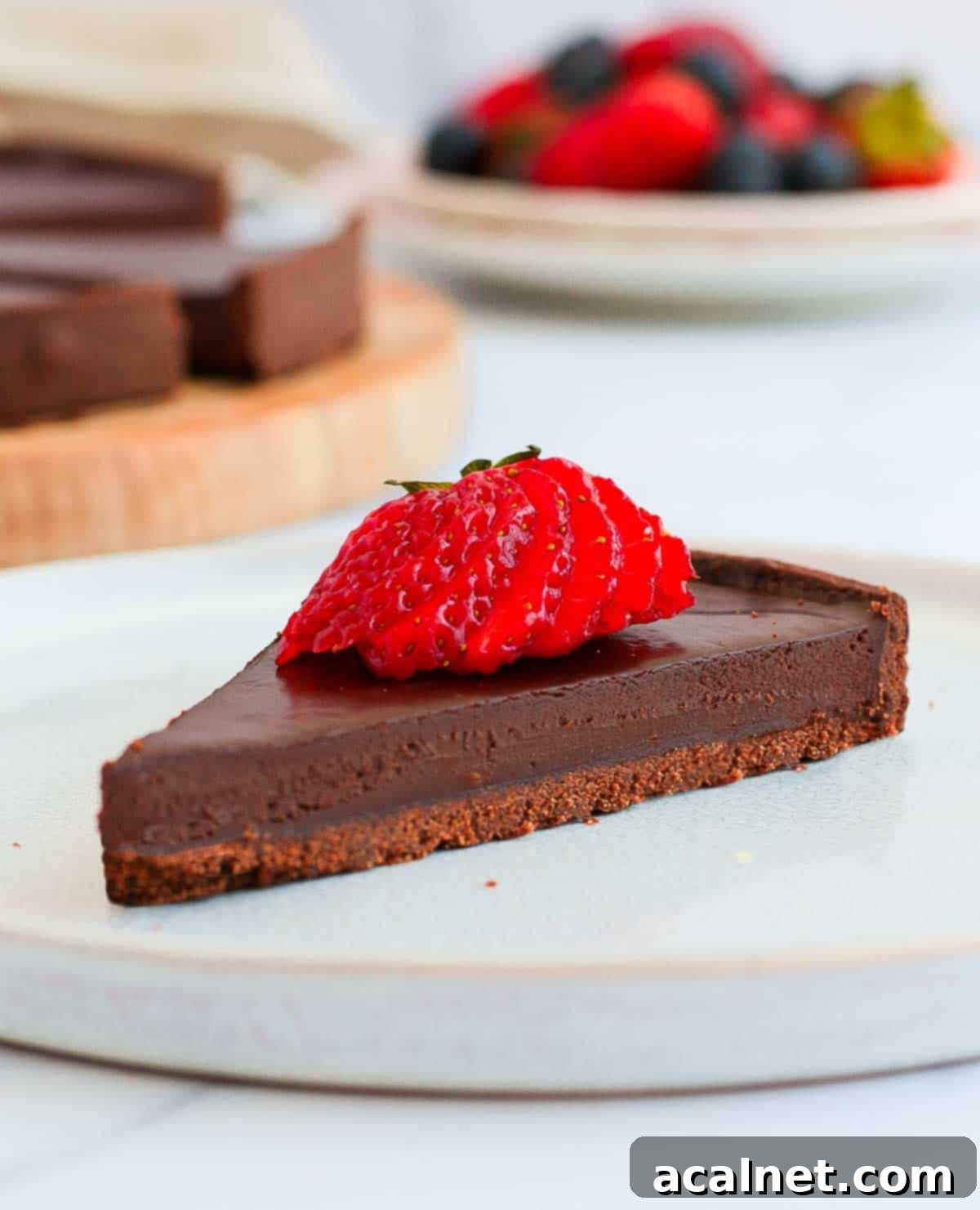 A slice of chocolate ganache tart topped with a strawberry on a white plate.