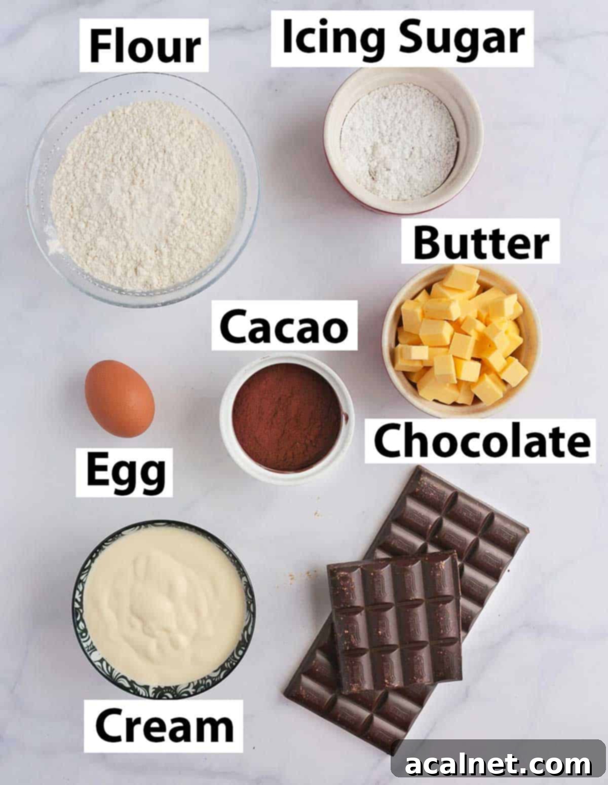Neatly arranged ingredients for a chocolate ganache tart, including flour, cocoa powder, butter, an egg, dark chocolate, and heavy cream on a white surface.