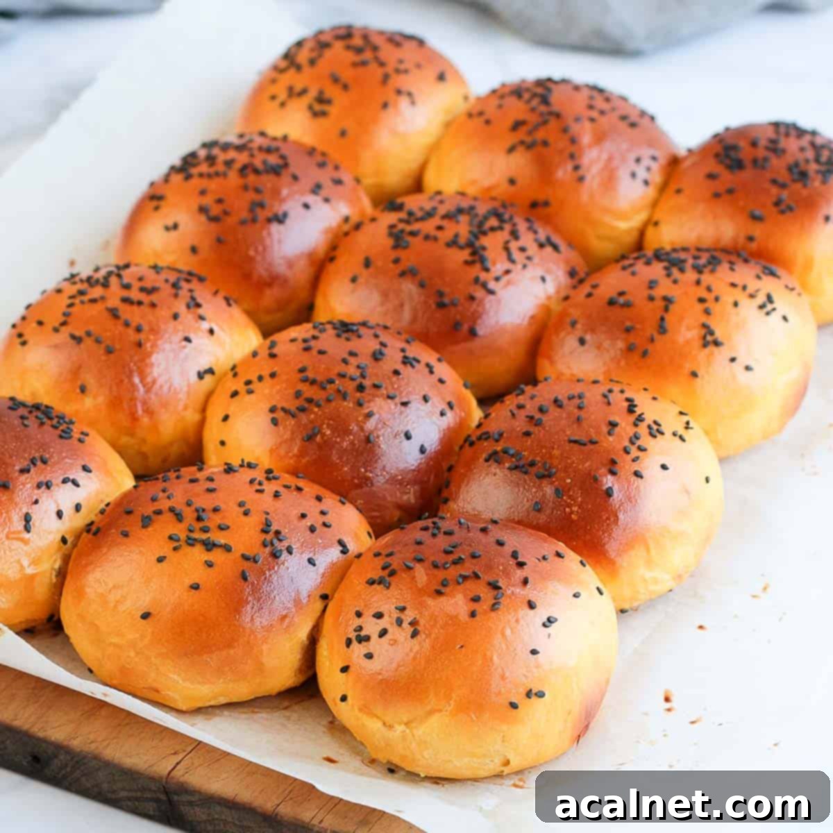 Freshly baked sweet potato buns resting on a sheet of baking paper over a rustic wooden cutting board, ready to be served.