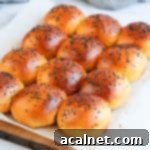 Buns on a sheet of baking paper over a wooden cutting board.