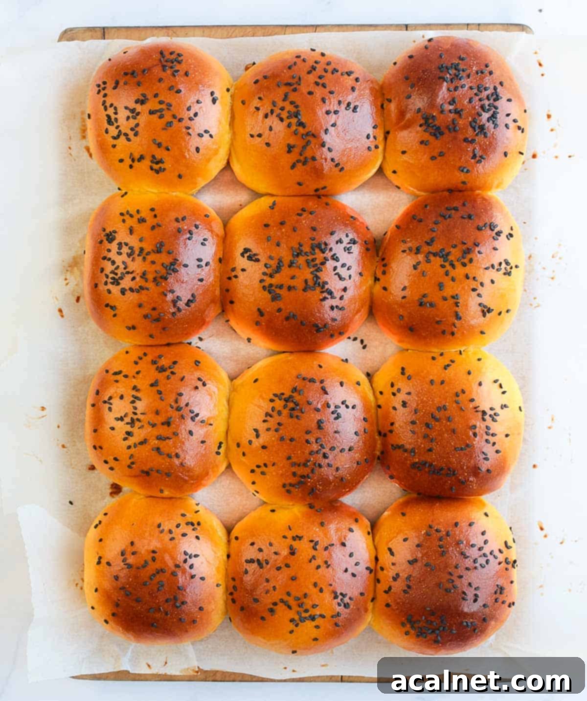 A tray of freshly baked, golden-brown sweet potato bread rolls cooling on baking paper over a rustic wooden cutting board, viewed from above.