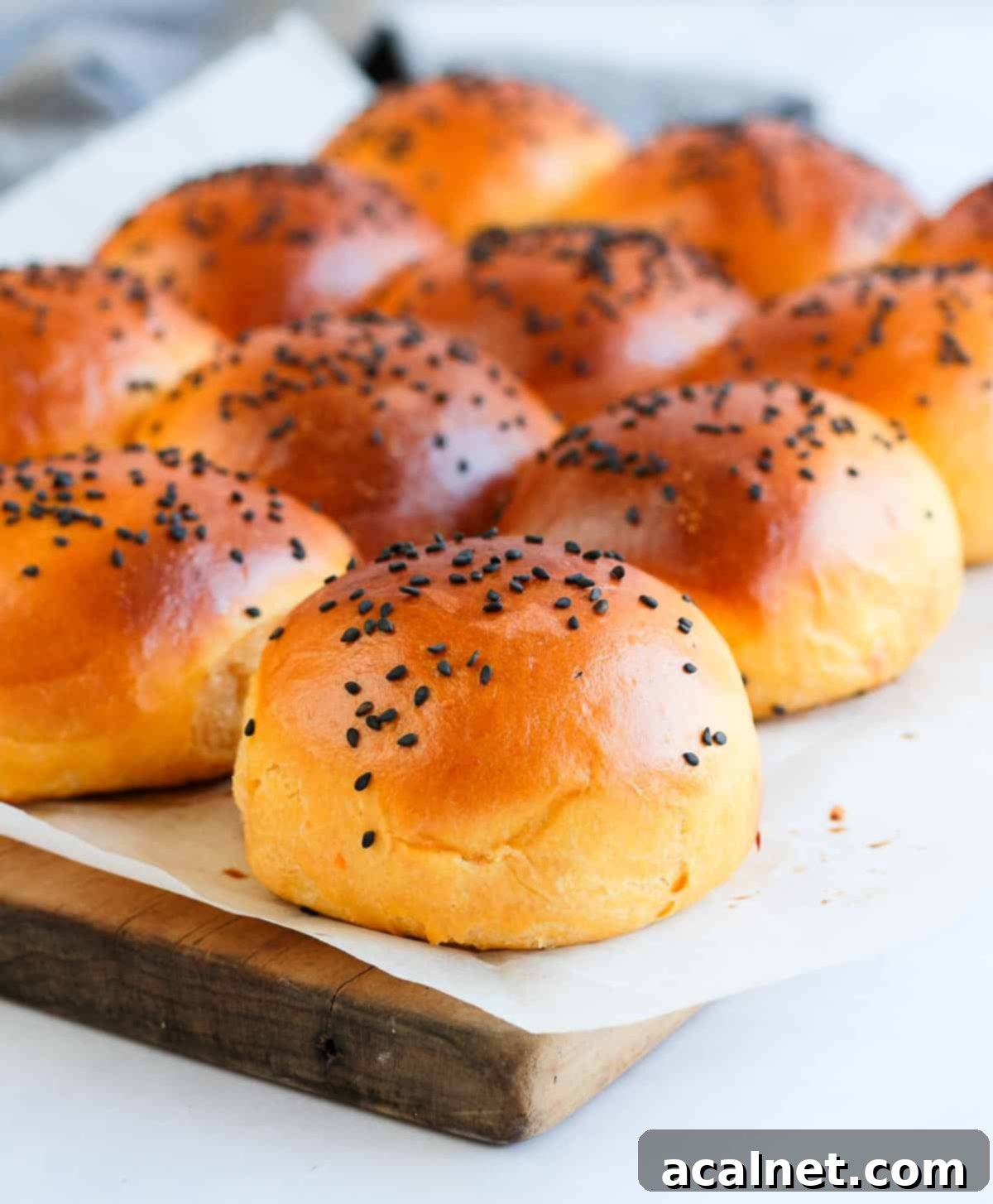 Close-up shot of a single sweet potato bun on baking paper, highlighting its golden crust and soft texture, set against a wooden board.