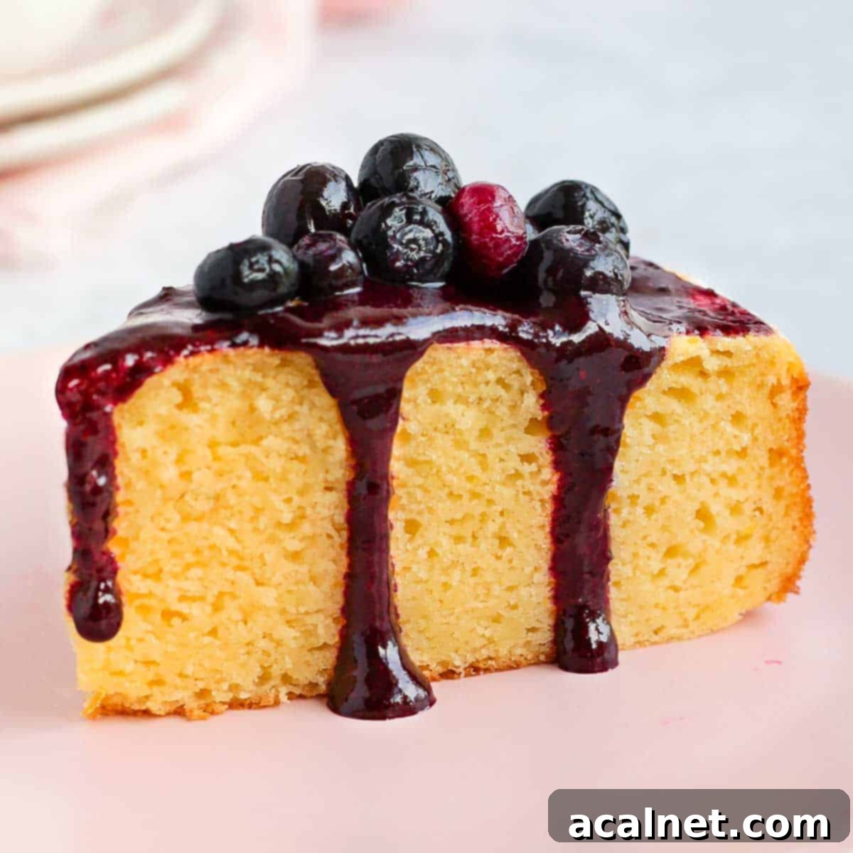 A slice of cake generously drizzled with the vibrant homemade blueberry coulis, showcasing its smooth texture and rich color.