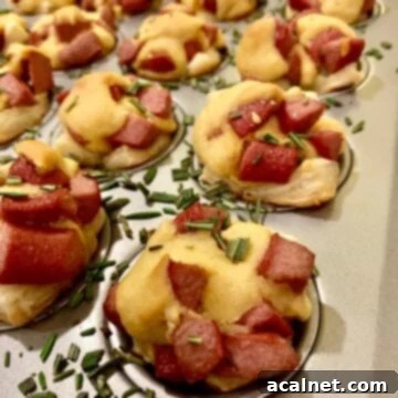Corn dog nuggets in a mini-muffin pan with rosemary sprinkled on top.