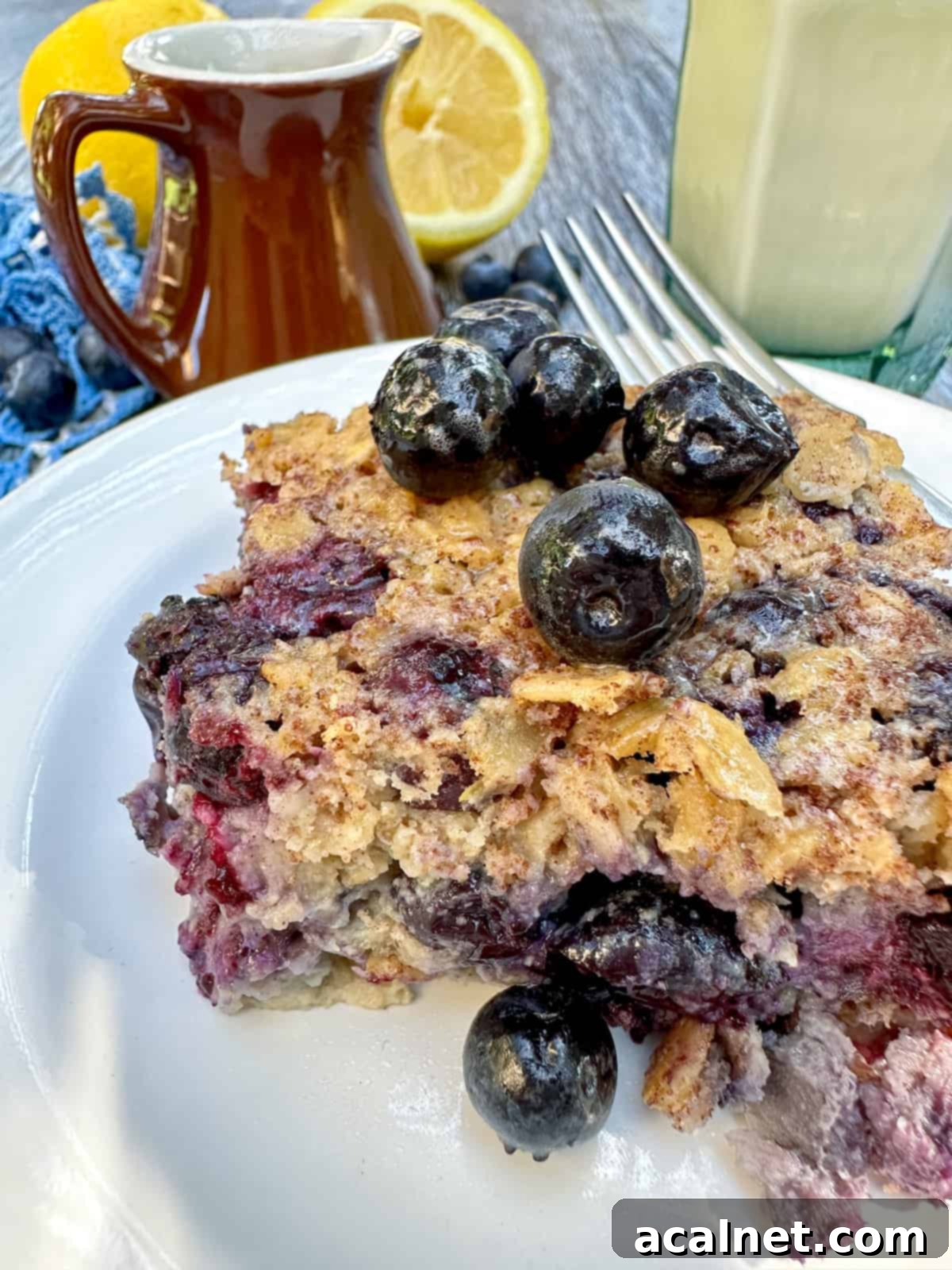 One portion of baked oatmeal with blueberries on the plate and on top with a wedge of lemon in the background.