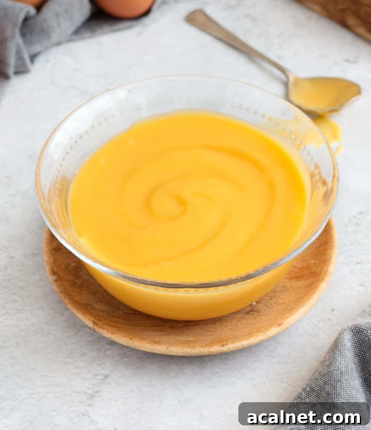 Zesty Lemon Delight 4 Rich, glossy lemon curd served in a clear glass bowl, resting on a rustic wooden plate.