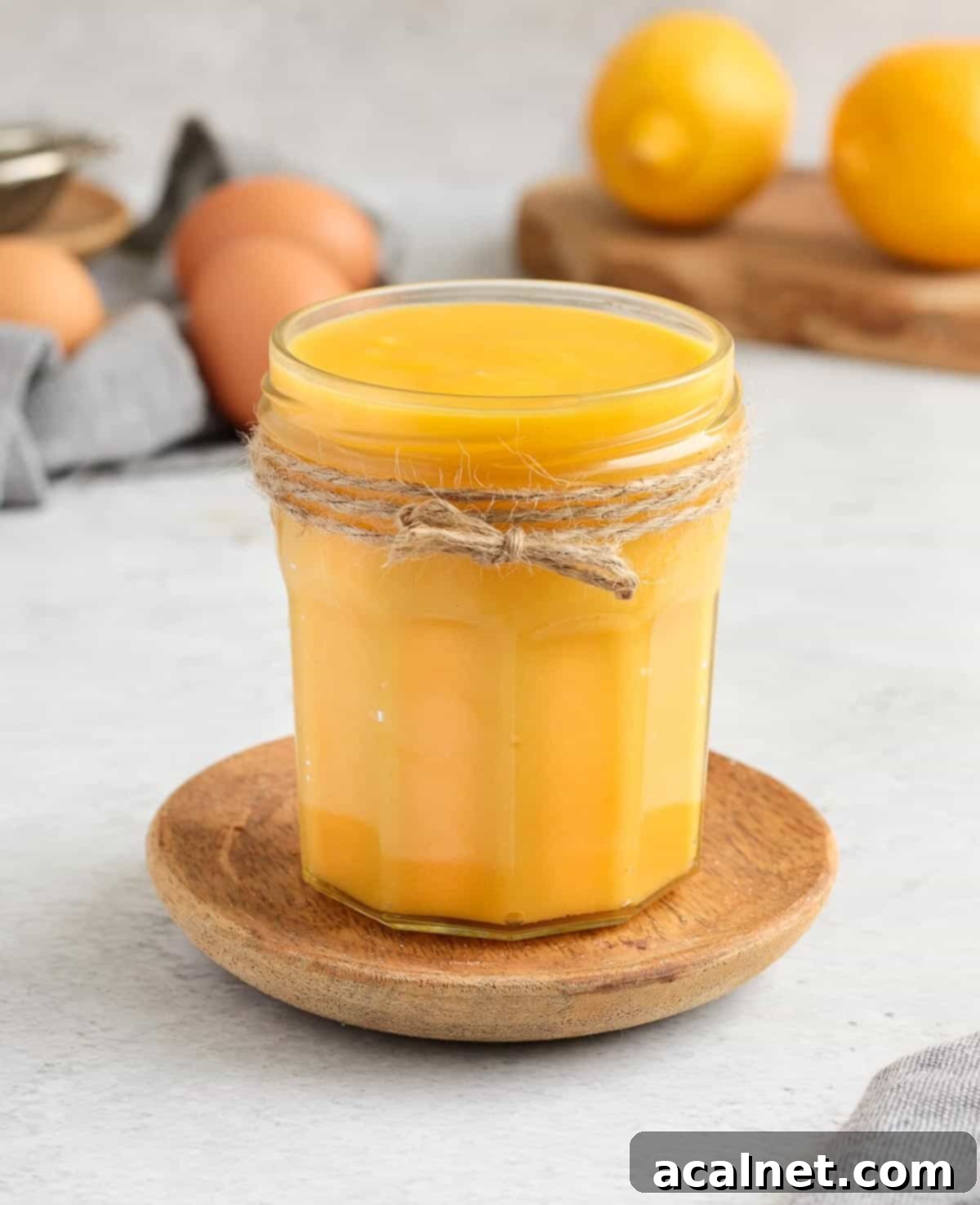 Zesty Lemon Delight 7 A glass jar brimming with smooth lemon curd, surrounded by fresh lemons and eggs in the background, hinting at the fresh ingredients.