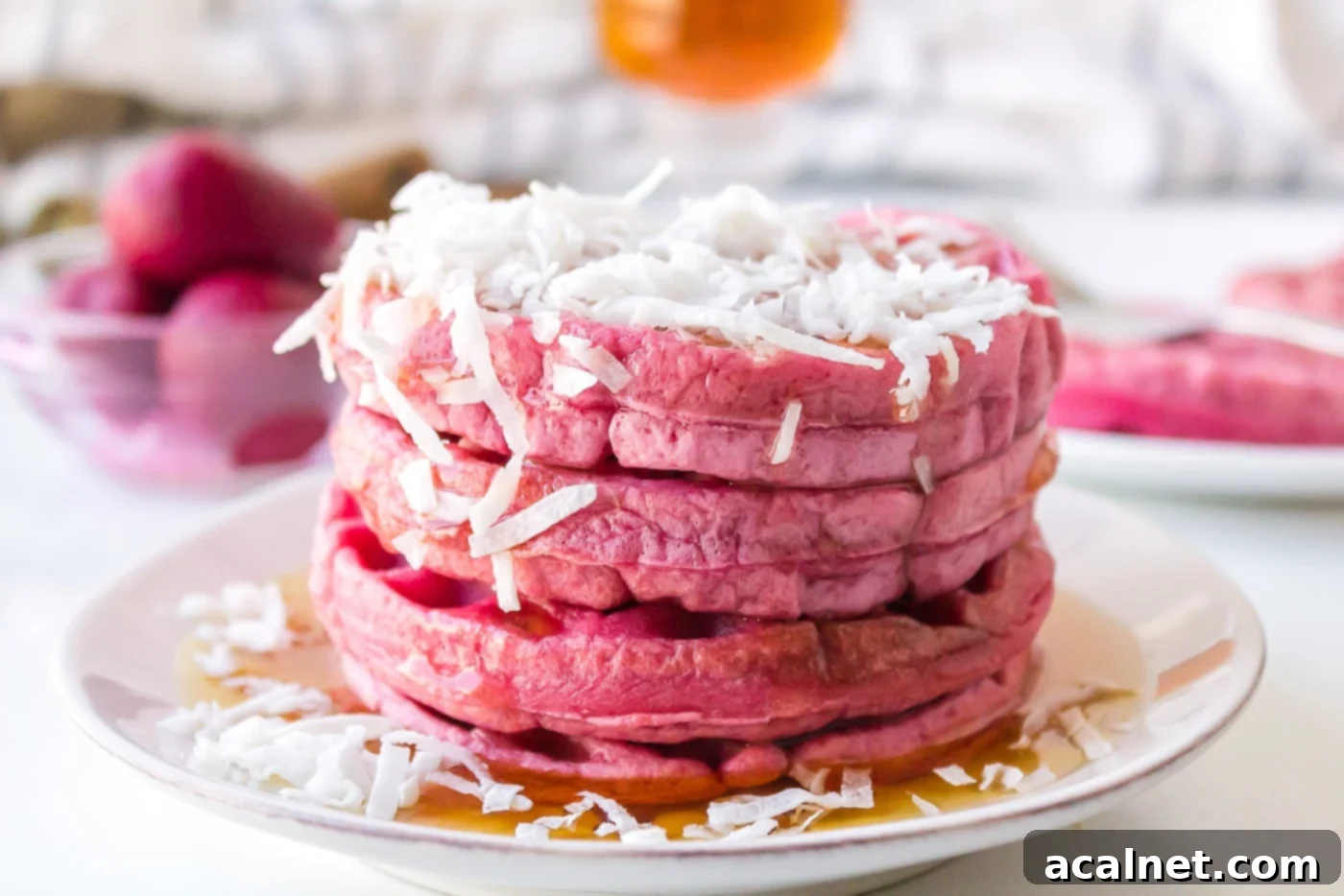 Fluffy pink waffles stacked with berries and syrup.