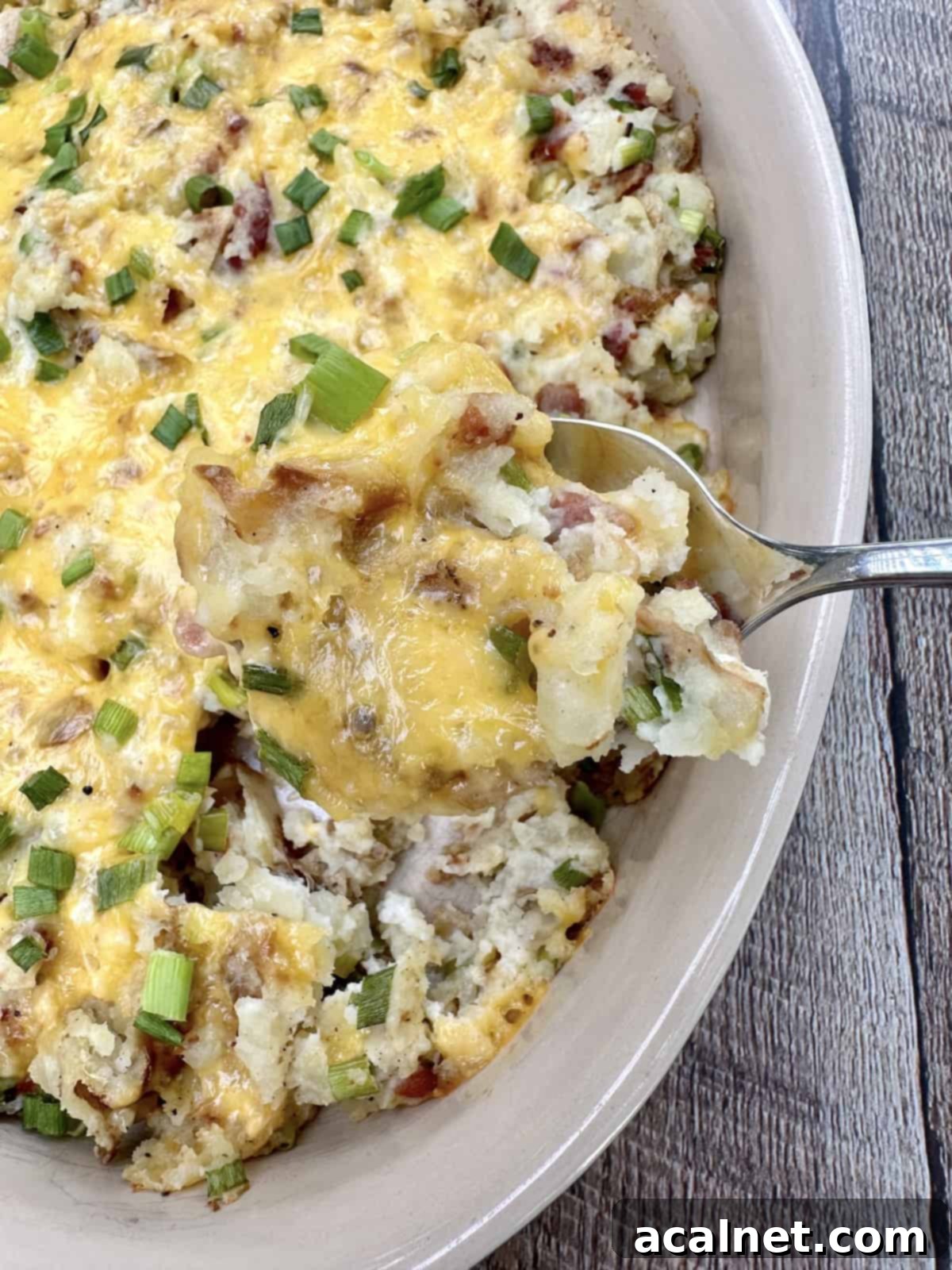 An up close shot of a spoon scooping up twice baked potatoes from a baking dish.