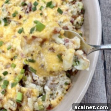 A spoon scooping up twice baked potatoes from a baking dish.
