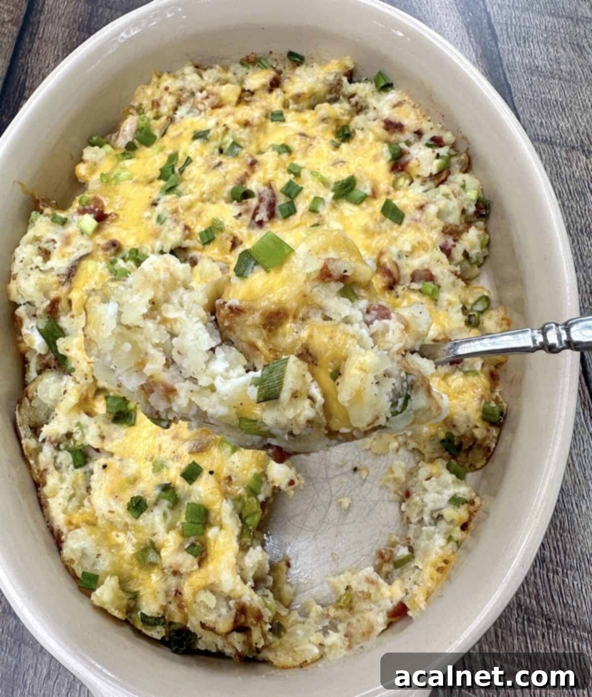 A large baking dish filled with twice baked mashed potatoes and a spoon scooping up a serving.
