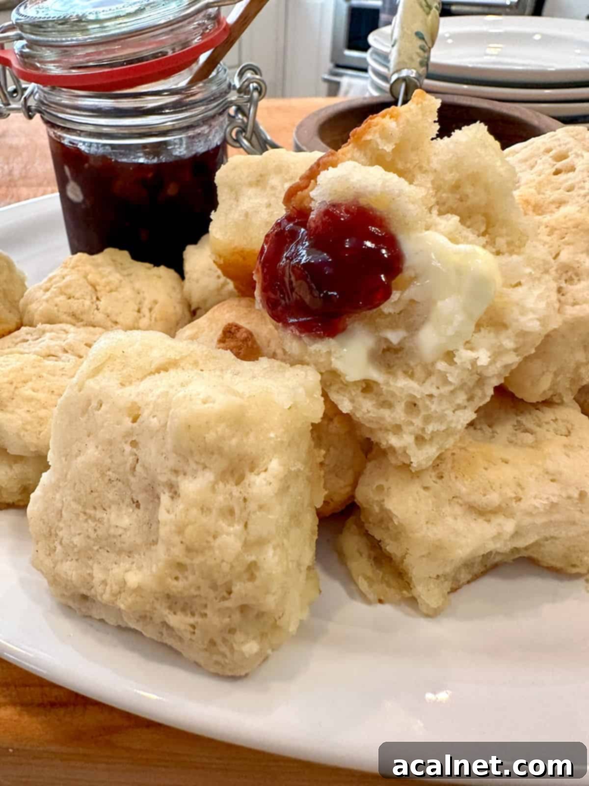 Freshly baked buttermilk butter biscuits arranged on a plate with a dollop of jam on one and a small jar of jam beside them.