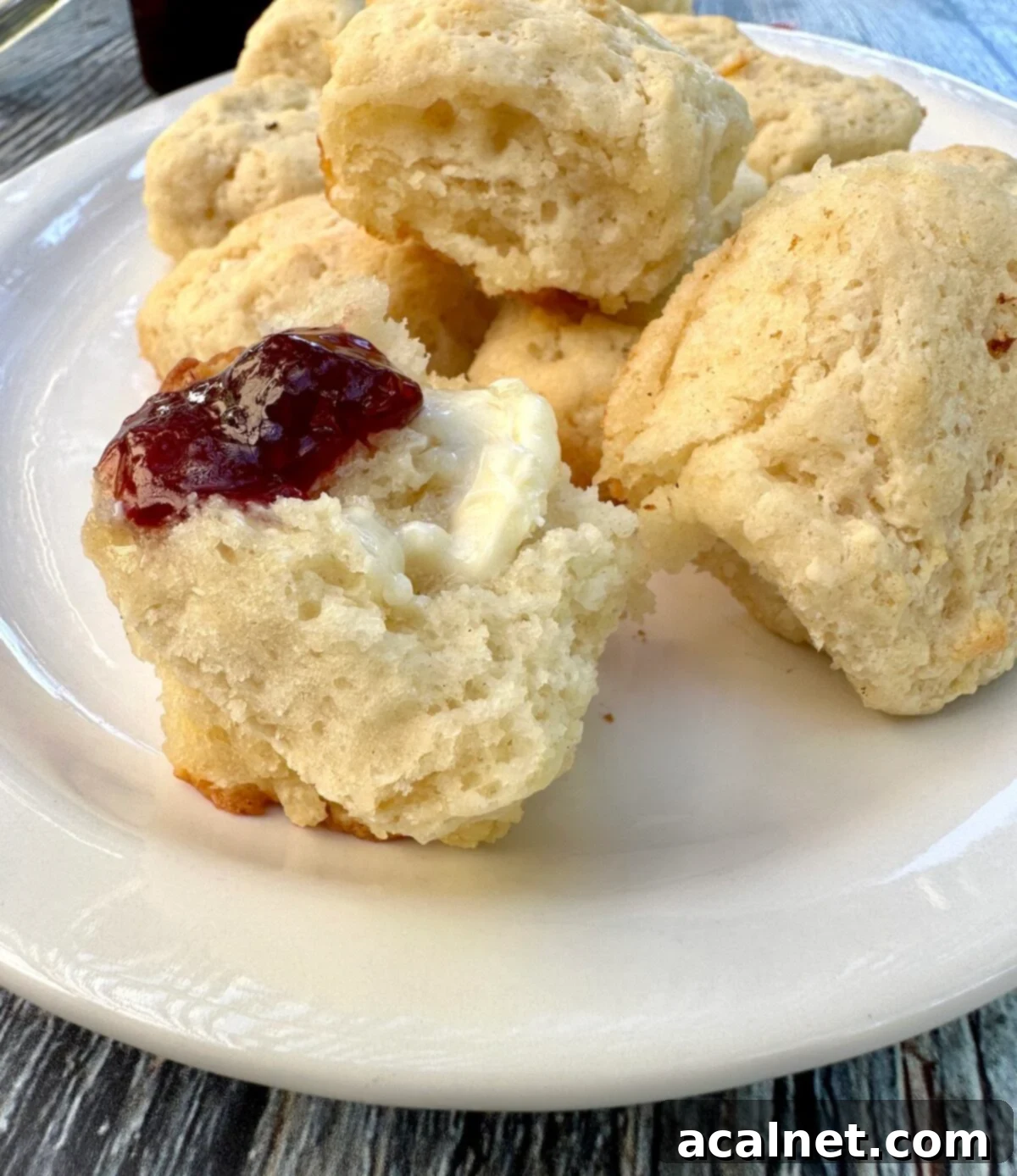 A plate of baked buttermilk butter biscuits, with one split open and spread with jam and butter.