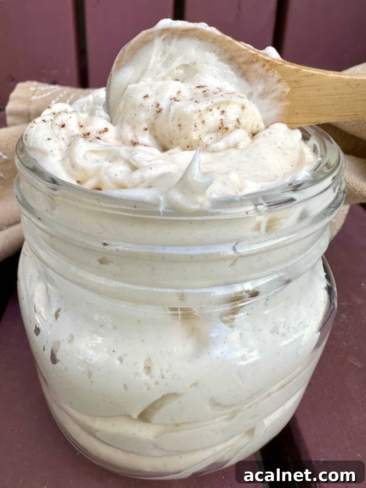 A charming small jar filled with fluffy whipped honey butter, with a wooden spoon nestled on top, ready to be wrapped as a thoughtful gift for friends or family.