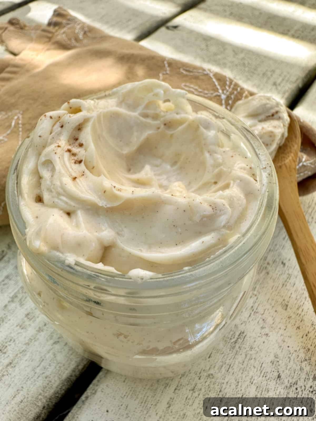 Freshly whipped honey butter in a small jar, placed on a wooden table with a wooden spoon resting on the side, ready to be served or added to a breakfast spread.