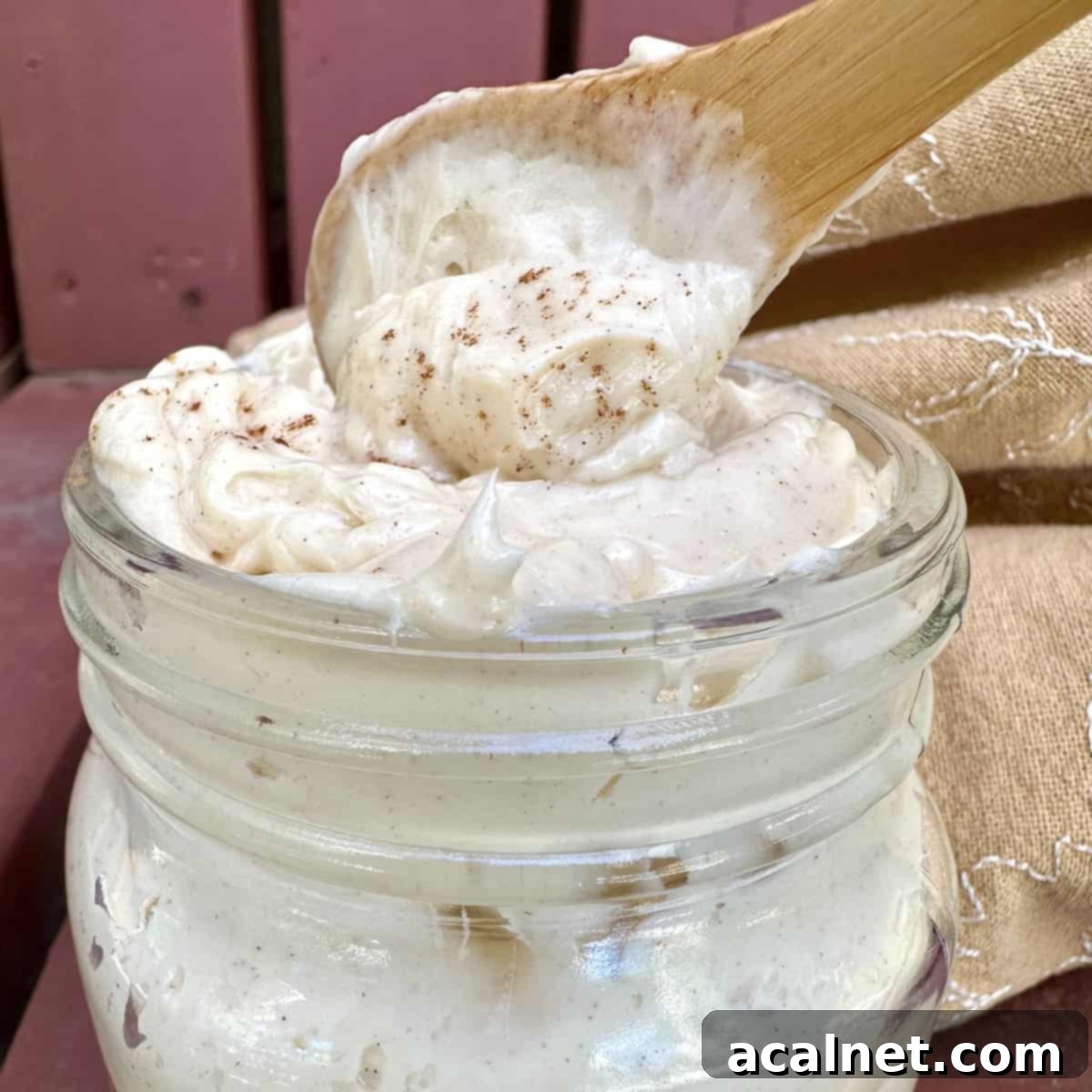A beautifully presented jar of perfectly whipped honey butter, topped with a wooden spoon scooping out a generous serving, highlighting its inviting texture.