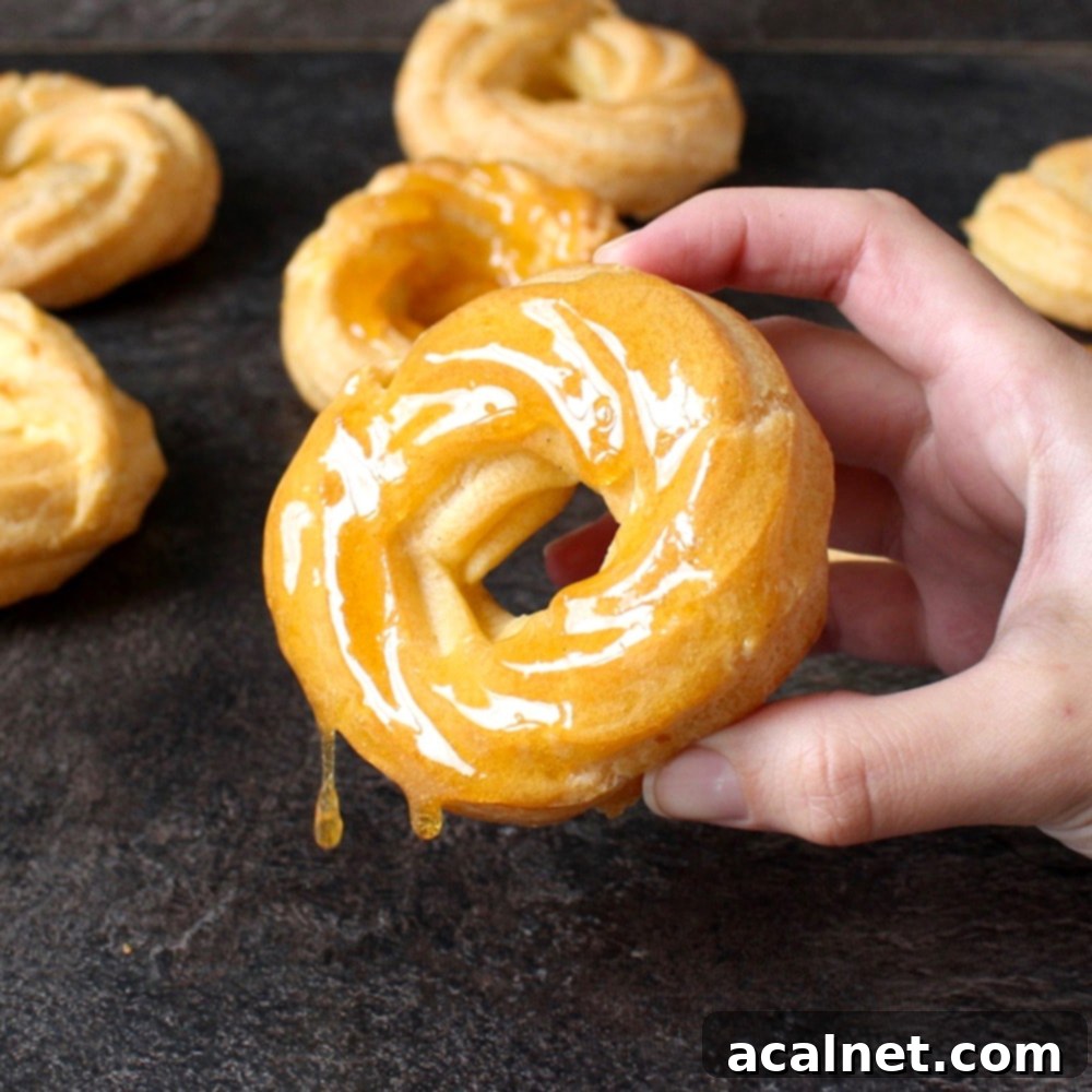 Honey Lemon Glazed French Crullers 2 A perfectly golden Honey Lemon Glazed Cruller Donut held gently in a hand, showcasing its unique ridged texture and glistening glaze.