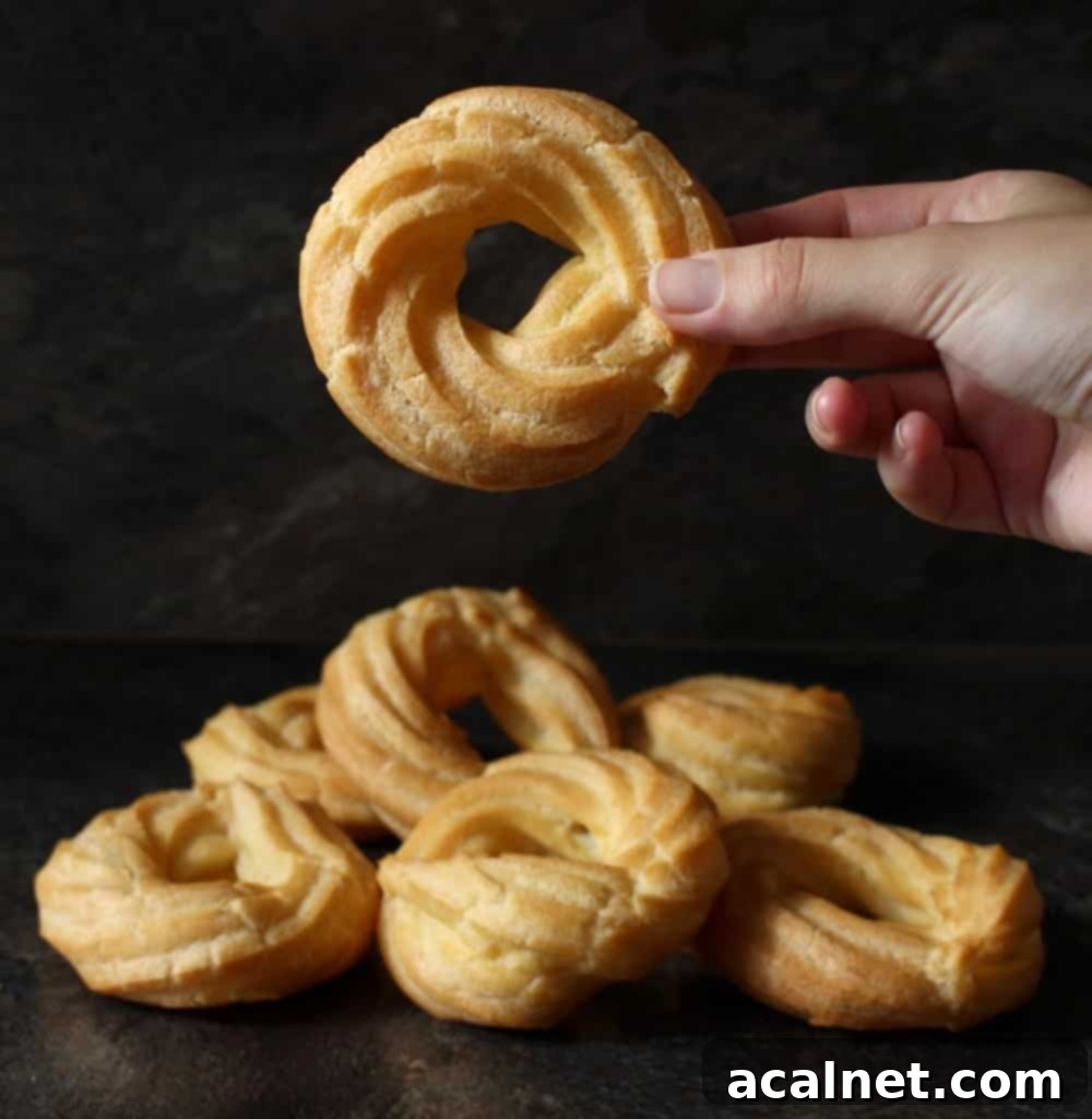 Honey Lemon Glazed French Crullers 3 A hand holding a single honey lemon glazed cruller donut above a stack of several crullers, highlighting their uniform shape and glaze.