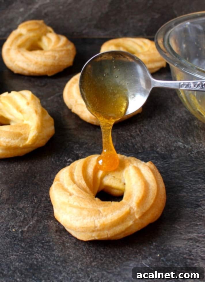 Honey Lemon Glazed French Crullers 6 Pouring a glistening honey lemon glaze from a spoon over a perfectly baked French Cruller Donut on a cooling rack.