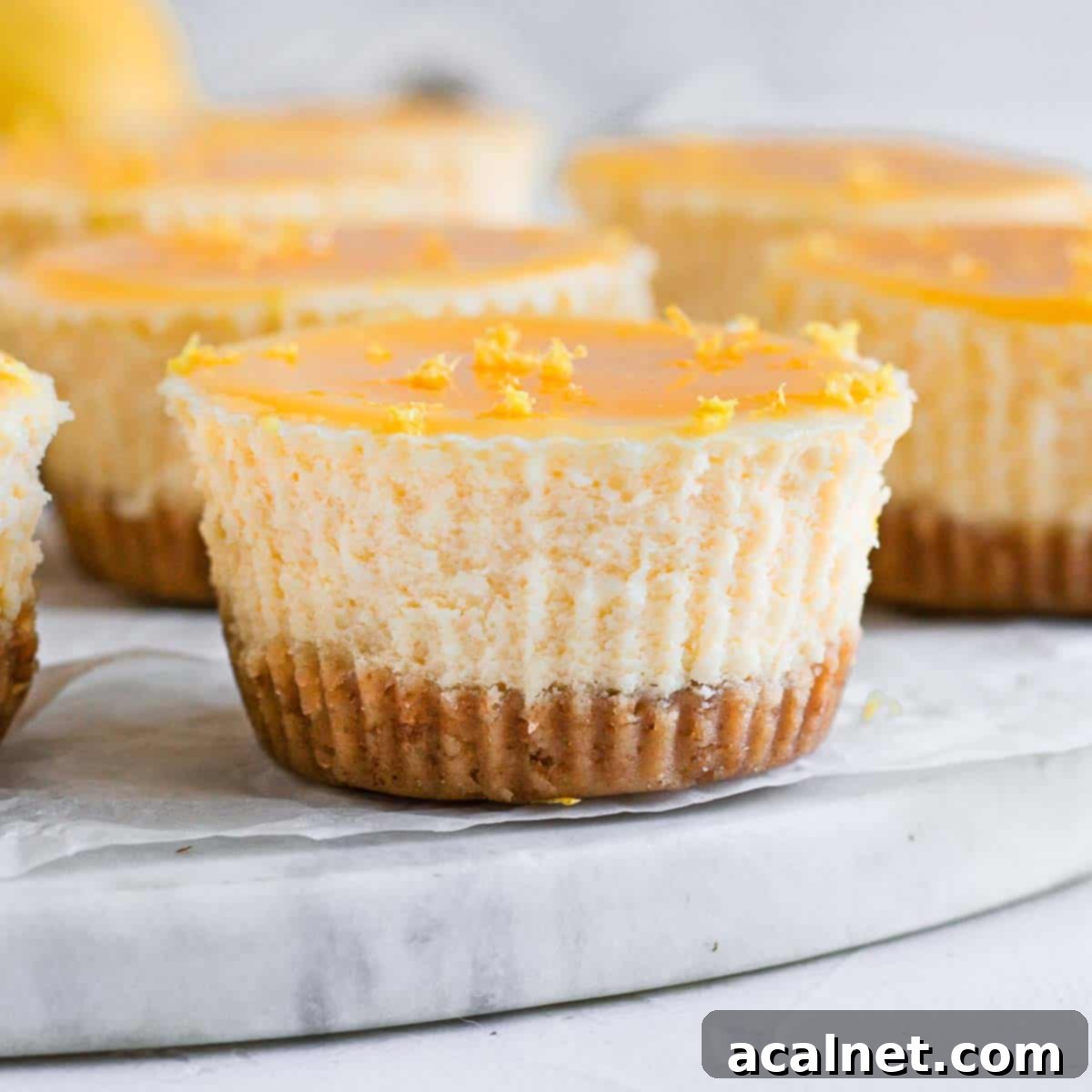 Zesty Mini Lemon Curd Cheesecakes 2 Close up on one mini lemon cheesecake over a marble board, showcasing its vibrant lemon curd topping and creamy texture.