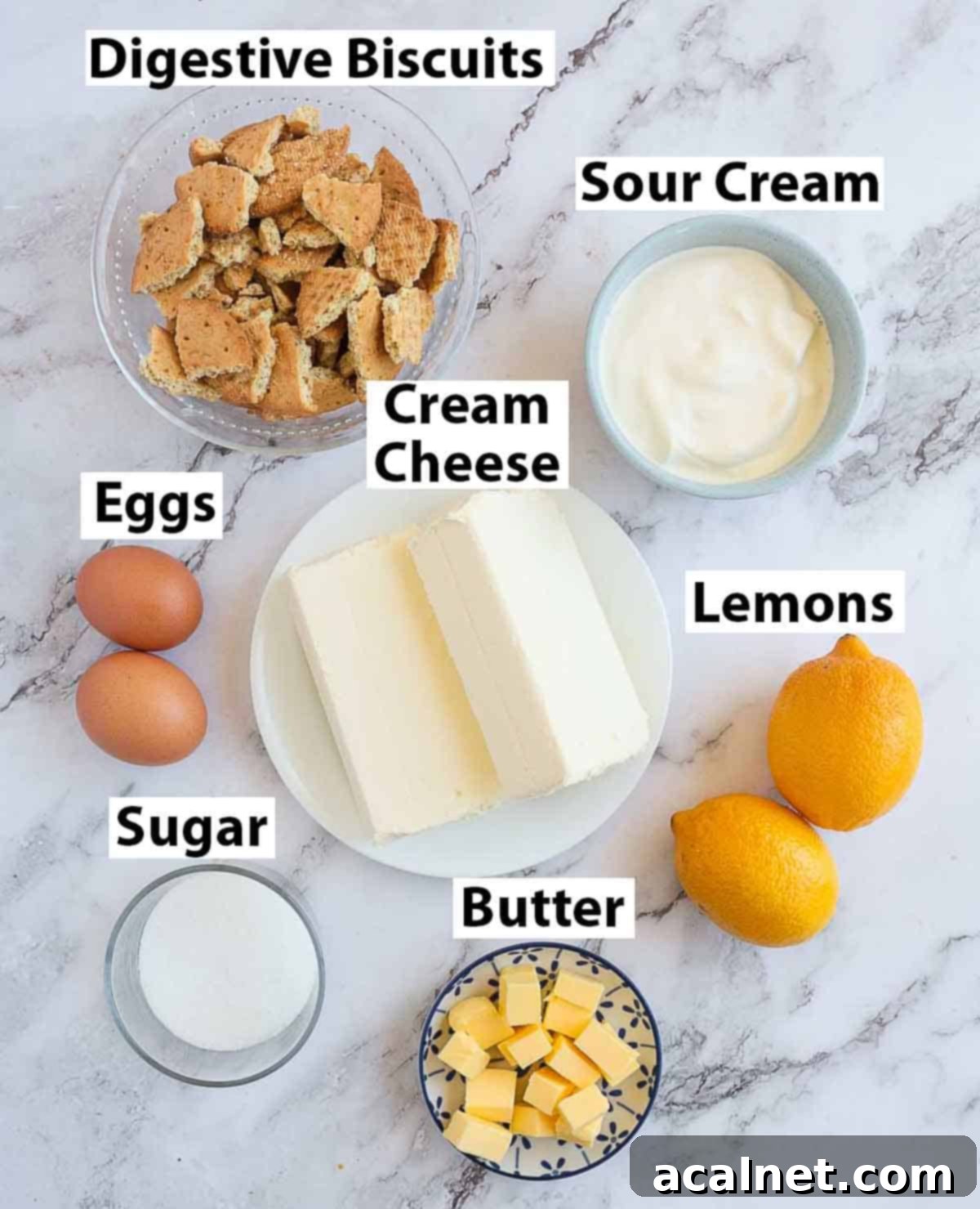Zesty Mini Lemon Curd Cheesecakes 3 Recipe ingredients laid out on a marble surface, including lemons, eggs, cream cheese, butter, and biscuits.