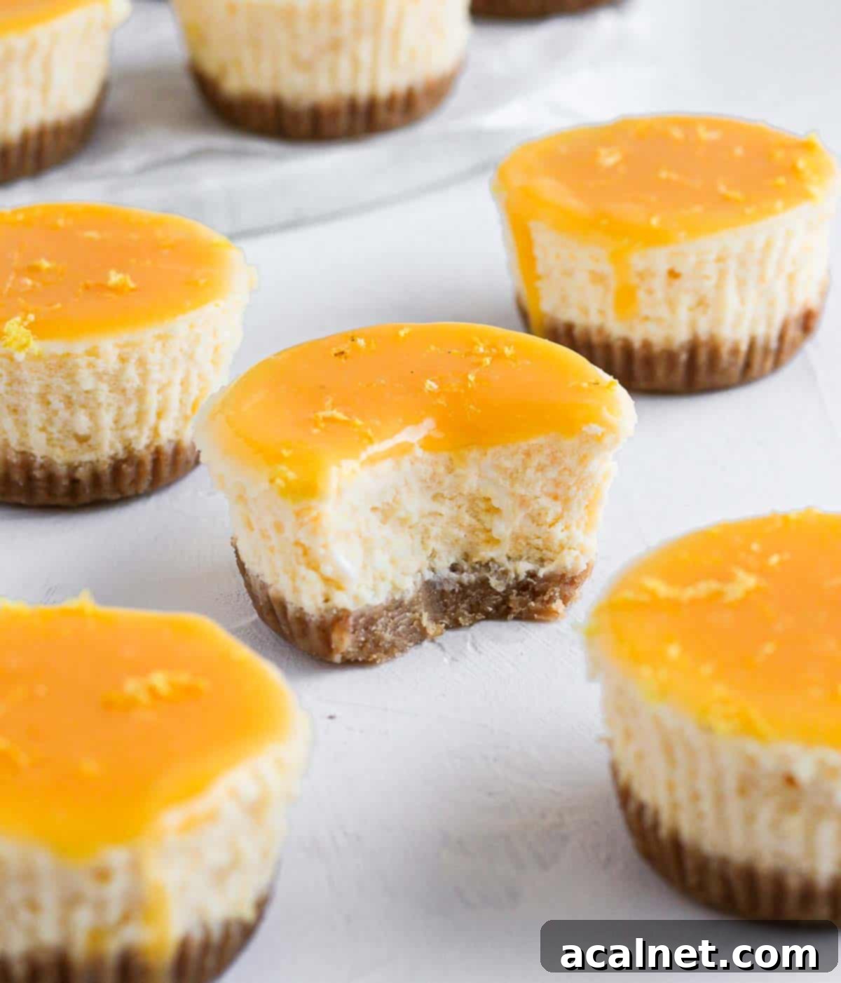 Zesty Mini Lemon Curd Cheesecakes 9 One mini lemon cheesecake with a bite taken off, showing its creamy filling and biscuit crust.