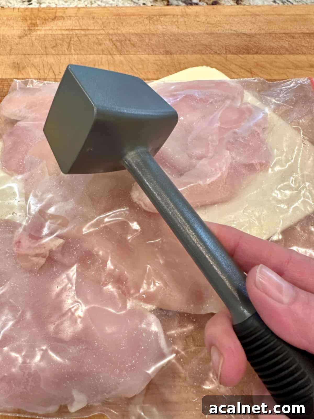 A meat mallet held over a plastic bag of sliced chicken, ready for tenderizing.