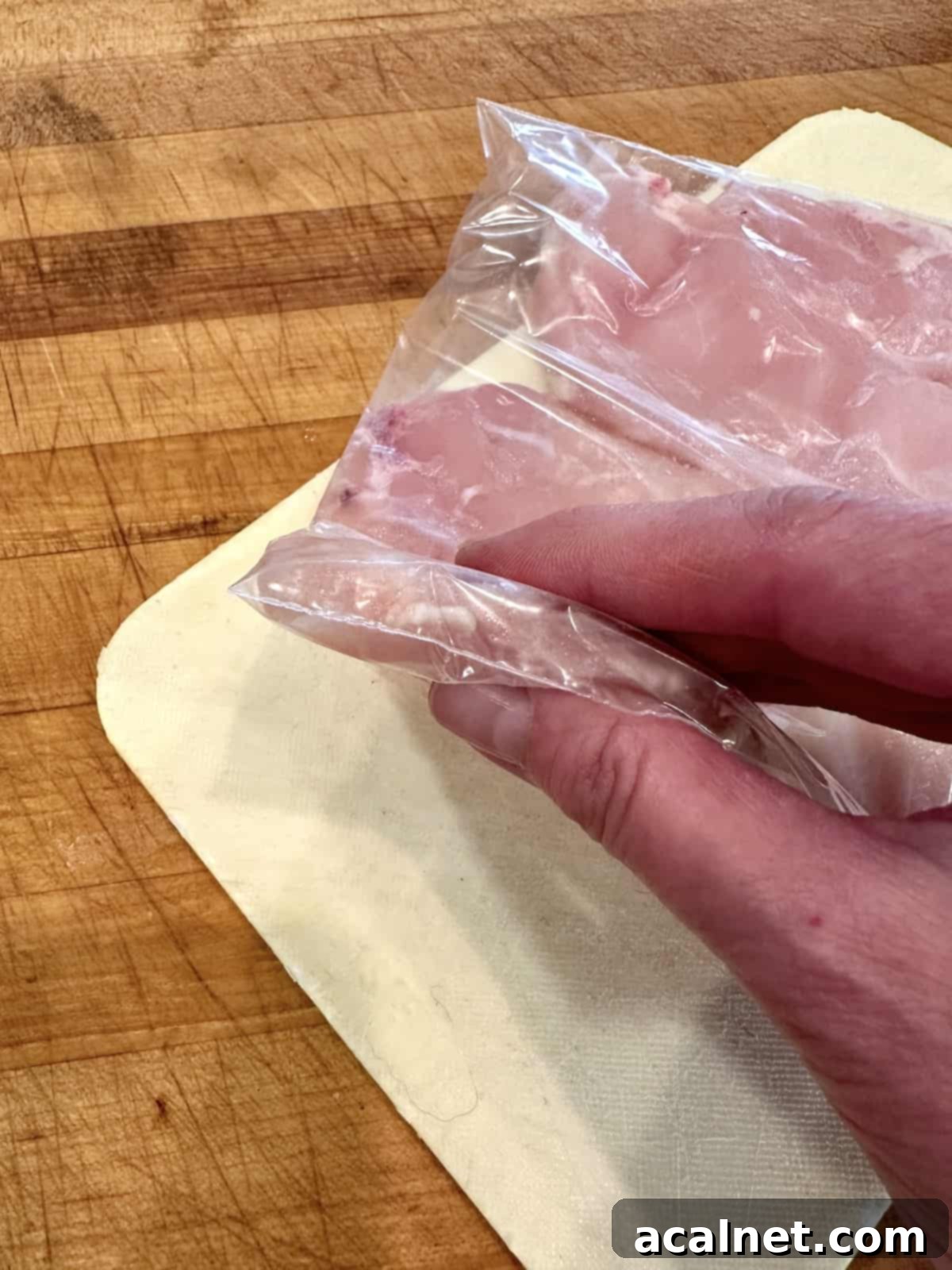 A thinly sliced and tenderized chicken breast in a plastic bag, held by a hand, showing uniform thickness.