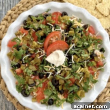 Five layered taco dip in a serving dish on a table with chips, highlighting its delicious layers.
