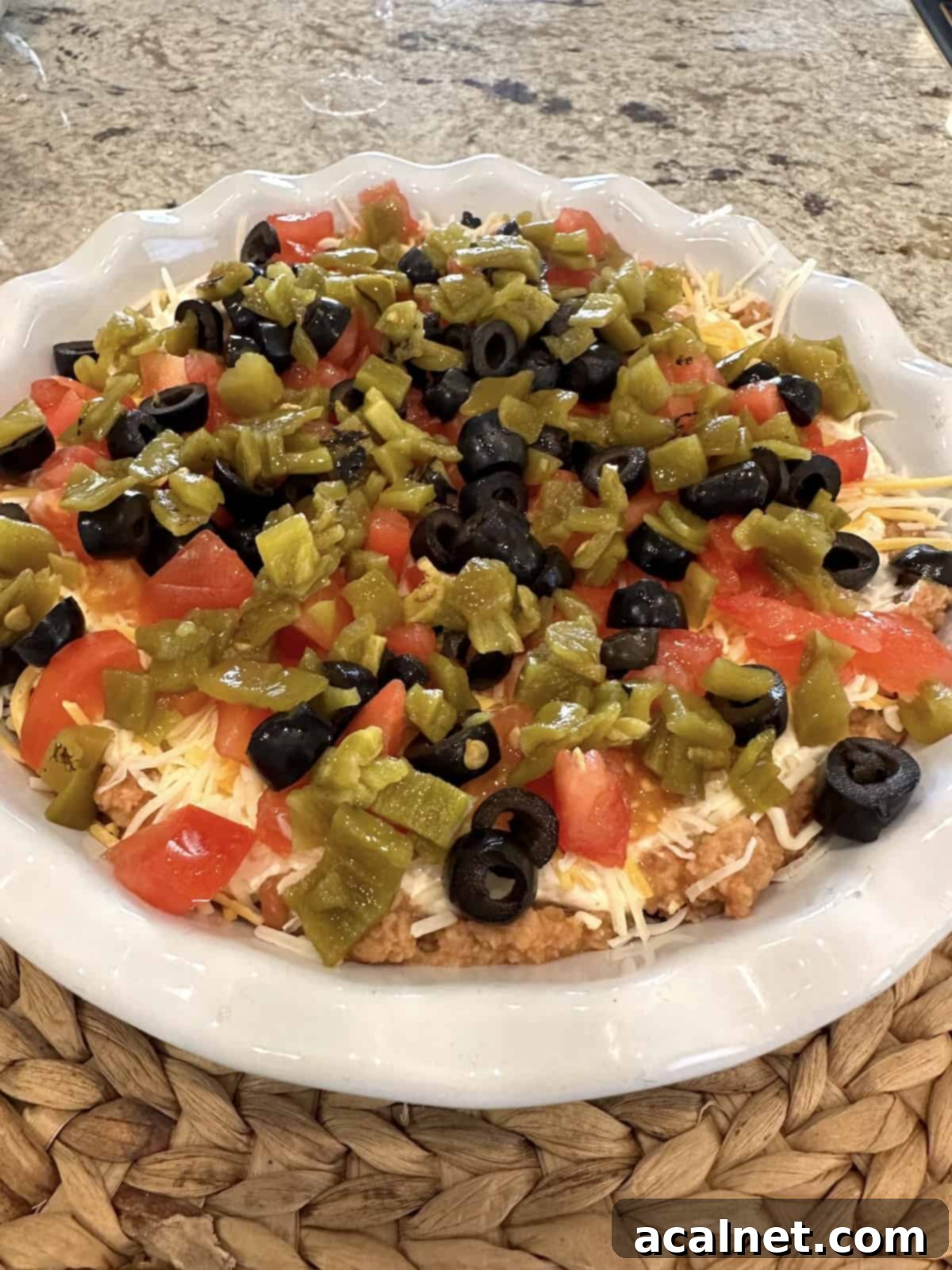 Fully assembled 5 layer taco dip in a dish, garnished with fresh cilantro on a kitchen counter.